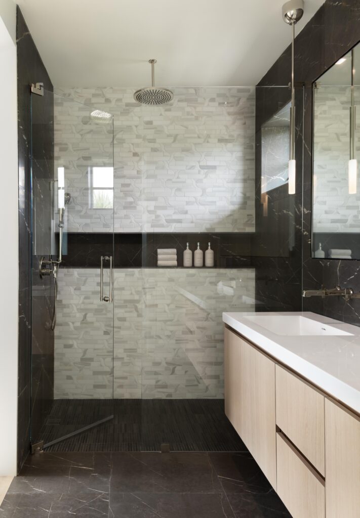 Guest en suite bathroom show with inset, full-length shelf, custom glass door, and rain showerhead.