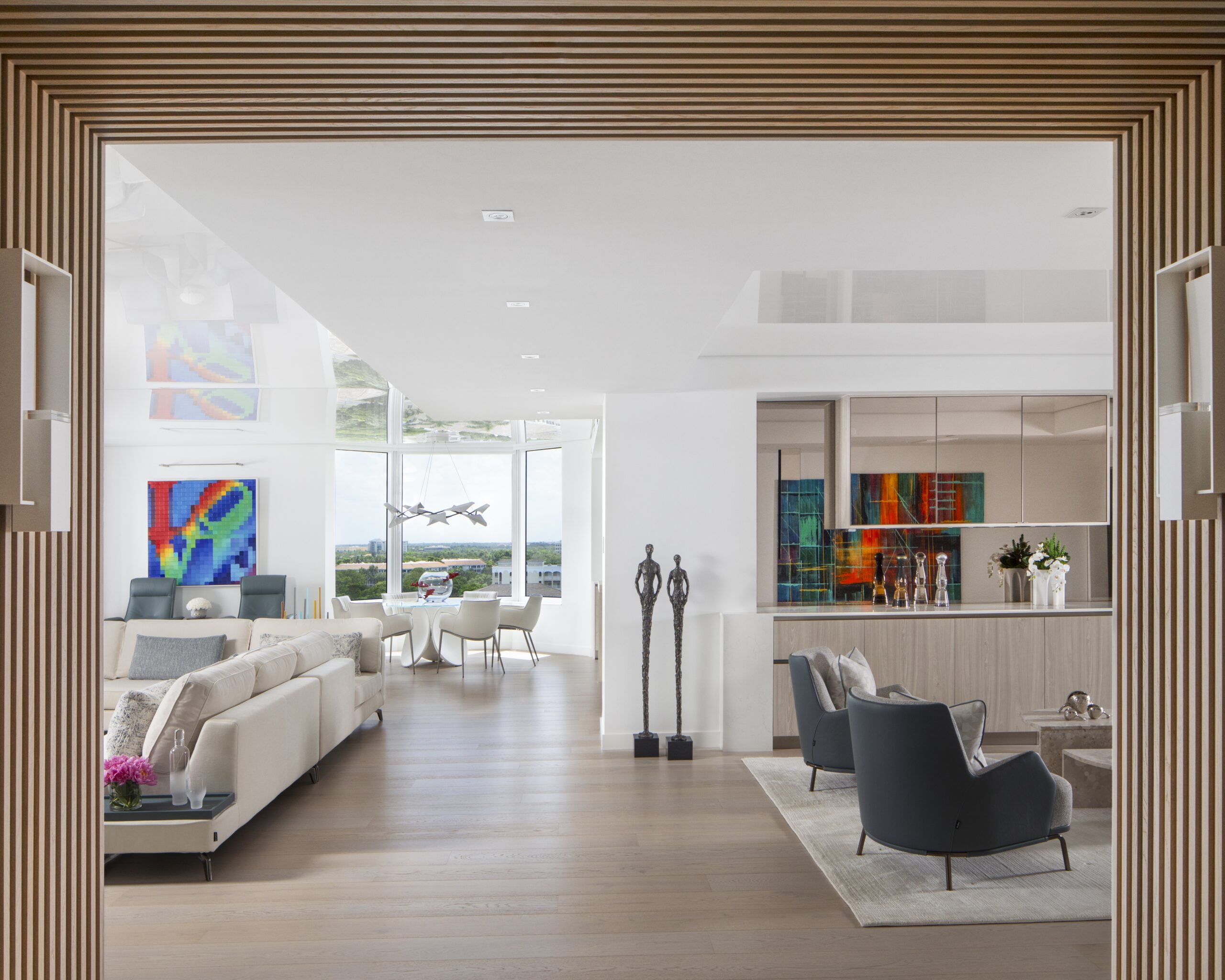 Modern luxury living room framed by wood slat feature wall with open-concept layout, neutral furnishings, and floor-to-ceiling windows overlooking a coastal city view