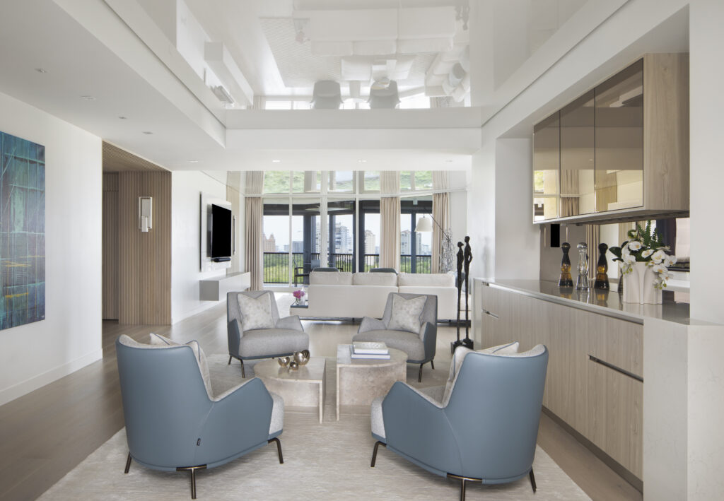 Open-concept living space with double-height ceilings, modern seating arrangement, and expansive glass doors leading to a balcony with skyline views