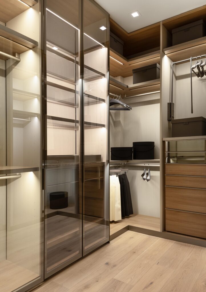 Luxury custom home primary suite closet with custom lighting, shelving, soft-close drawers, and glass doors.