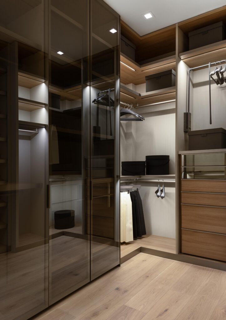 Luxury custom primary suite closet with custom lighting, handing space, drawers and glass doors.