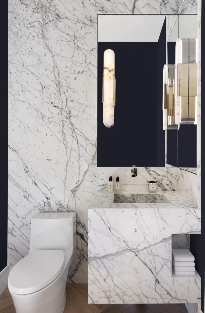 Custom marble wall and vanity in guest bathroom with herringbone patterned natural wood flooring.