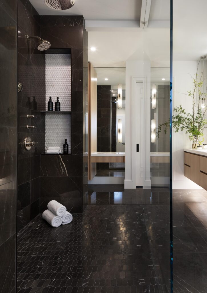 A luxury custom primary suite walk-in shower with dual showerhead, custom glass wall, and floating vanity.