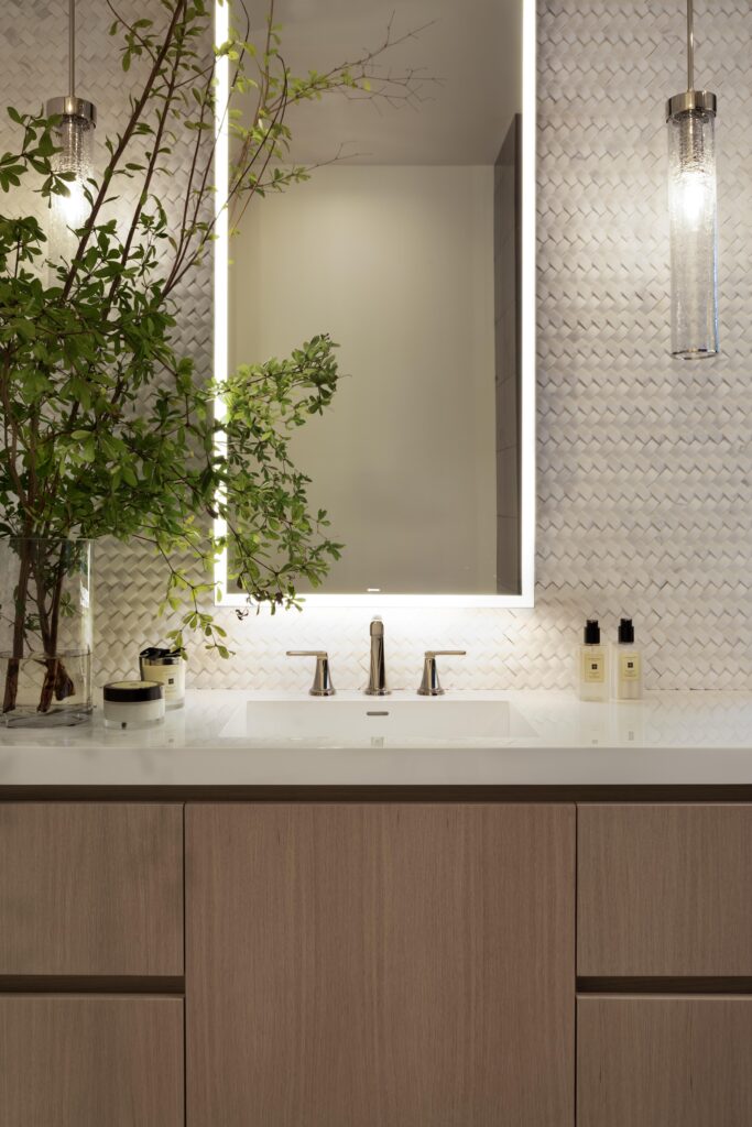 Custom built bathroom vanity with woven tile backsplash, hanging pendant lights and a lighted mirror.